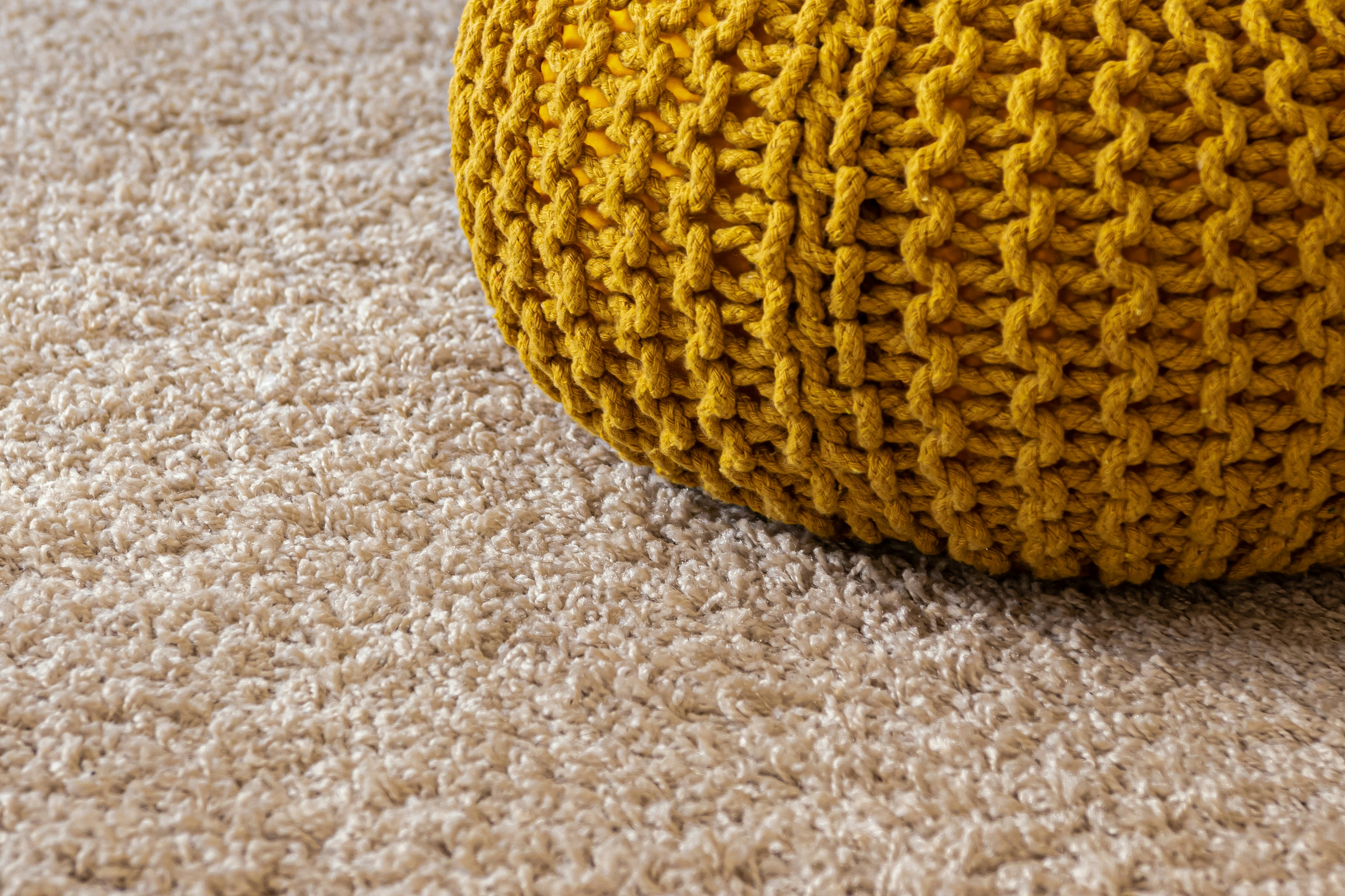 close up image of soft, plush, light beige carpet with yellow woven foot rest accent