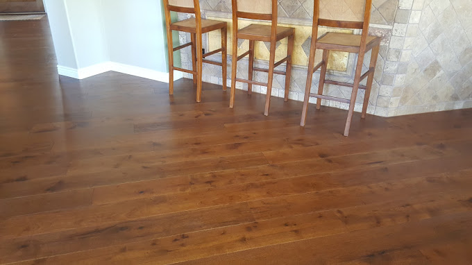 Warm oak luxury vinyl flooring with wood grain in kitchen with three wooden bar stolls and natural stone tile backsplash