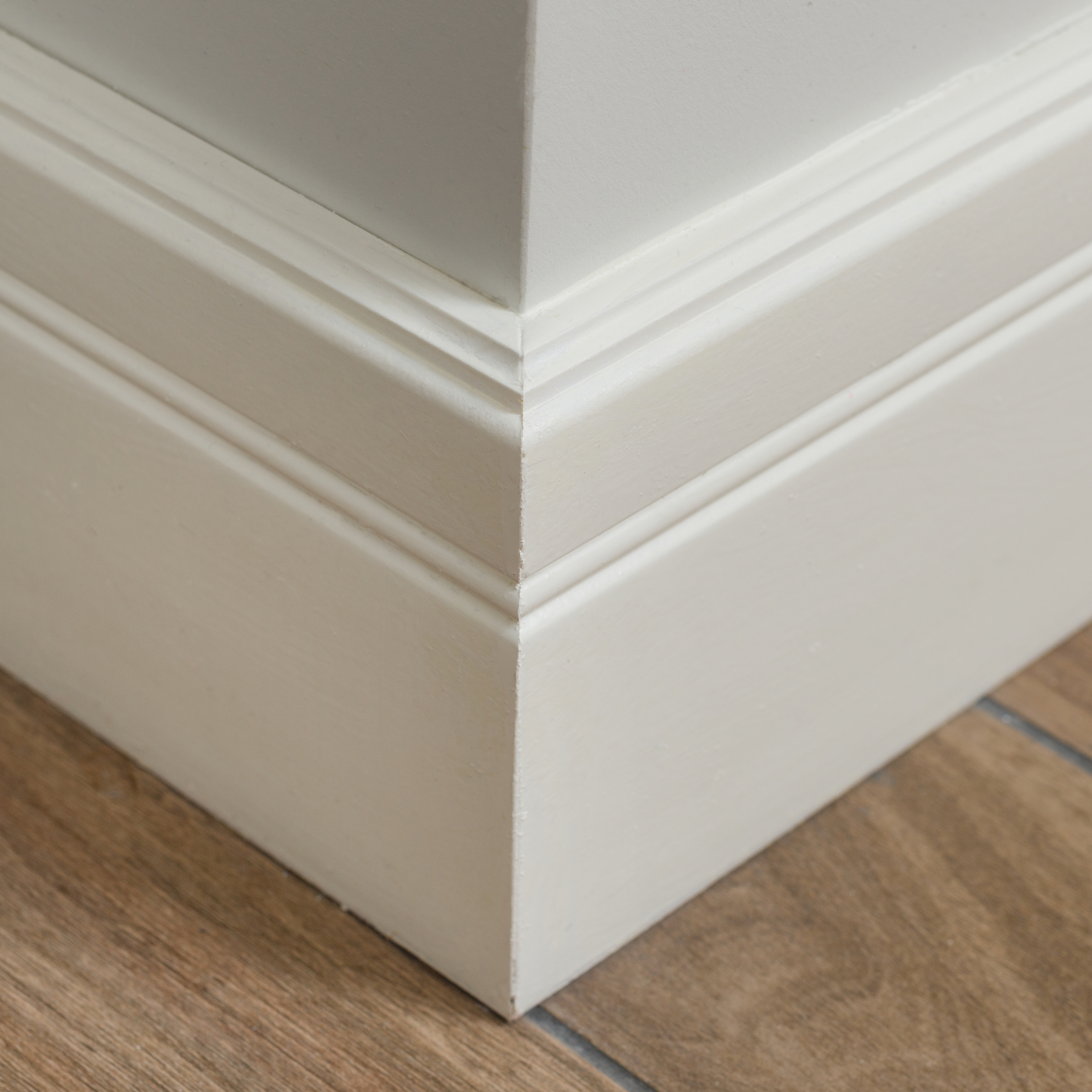 Close up photo of white crown molding baseboard with grey wall paint and light brown tile floor